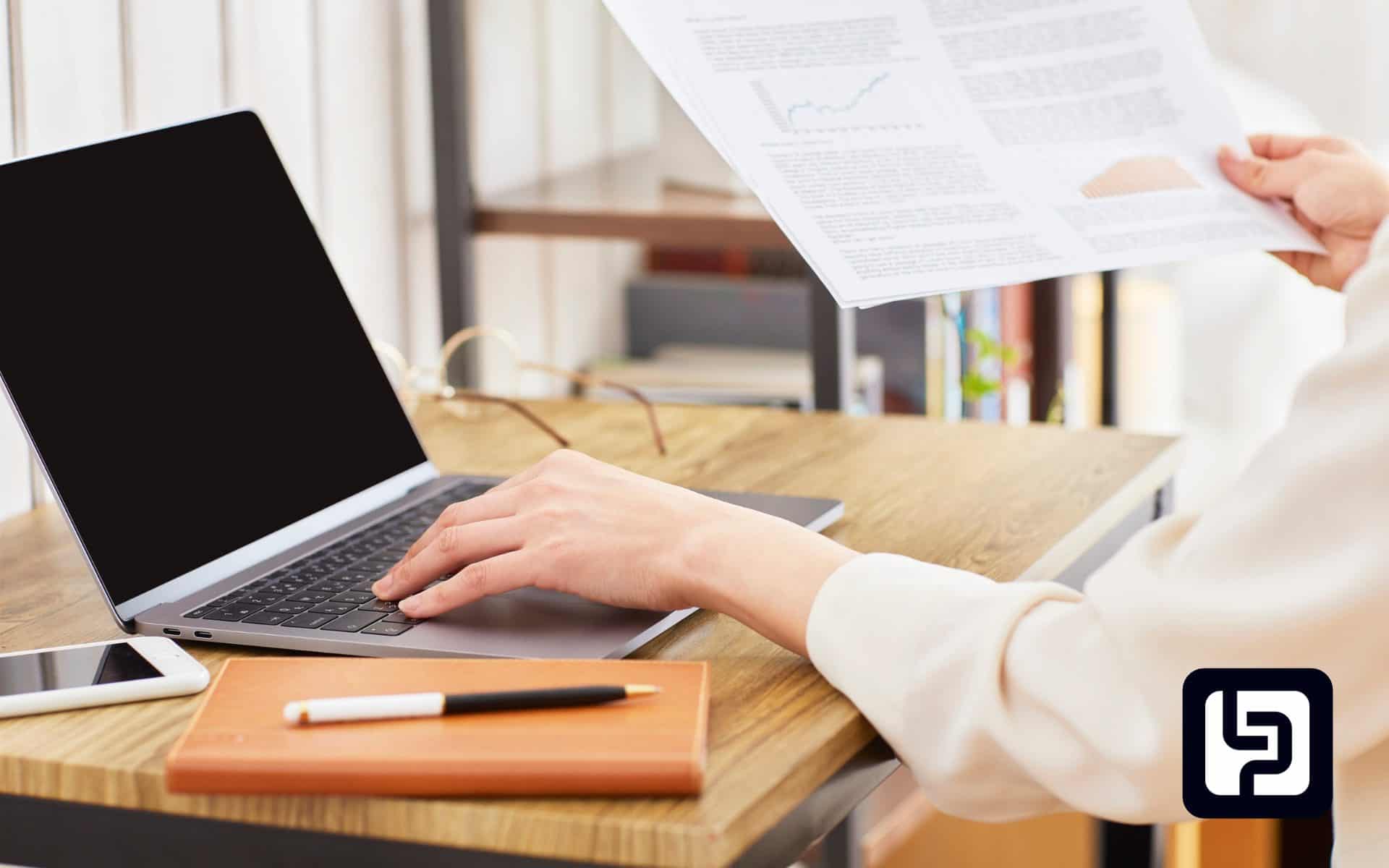 Hands on a laptop with a pen and notebook