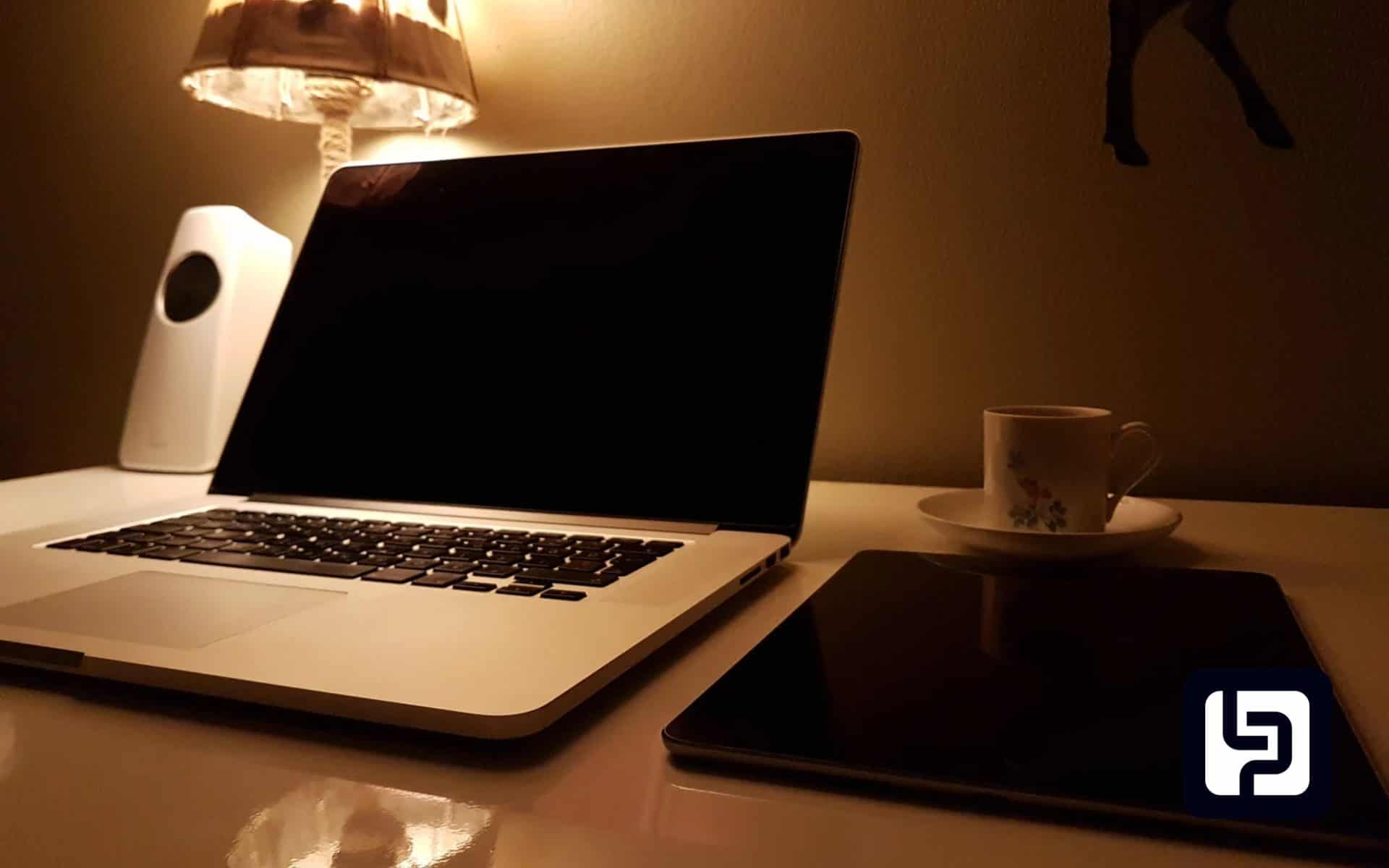 Home desk at night with a dark laptop and tablet beside a warm lamp